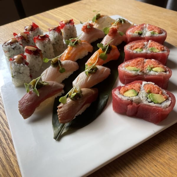 A white platter holds various sushi rolls and nigiri, including tuna, salmon, and white fish.
