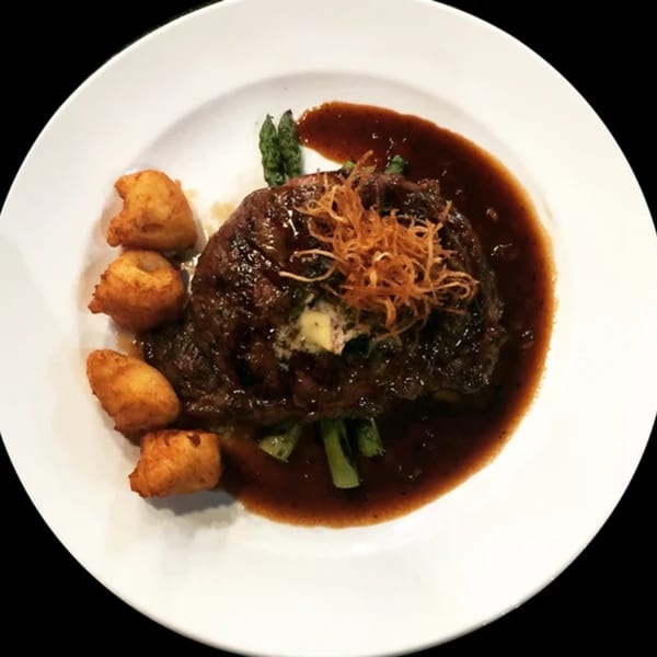 A steak with sauce, asparagus, fried potatoes, and crispy onions on a white plate.