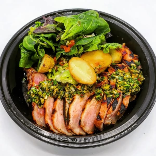 Seared duck breast with chimichurri, roasted potatoes, and a fresh green salad in a black bowl.
