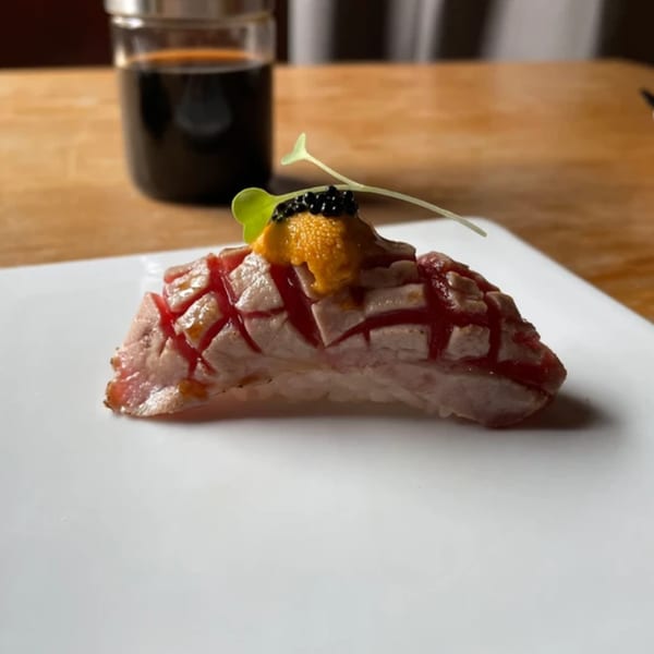 Elite Five Sushi & Grill's seared tuna nigiri with uni, caviar, and a microgreen on a white plate.