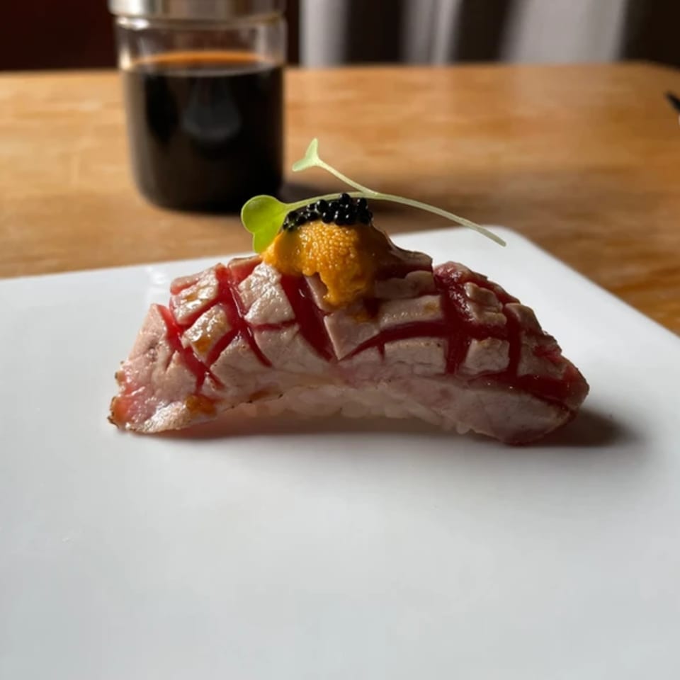 Elite Five Sushi & Grill's seared tuna nigiri with uni, caviar, and a microgreen on a white plate.