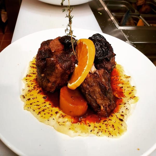 Braised short ribs with mashed potatoes, orange slice, and herbs on a white plate.