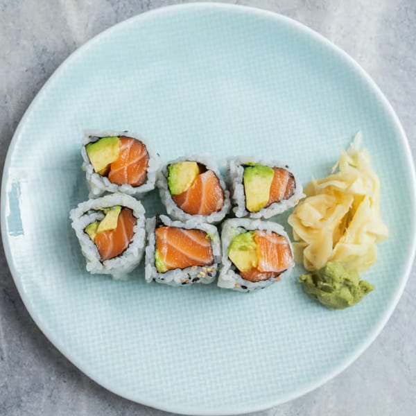 Six salmon and avocado sushi rolls with ginger and wasabi on a light blue plate.